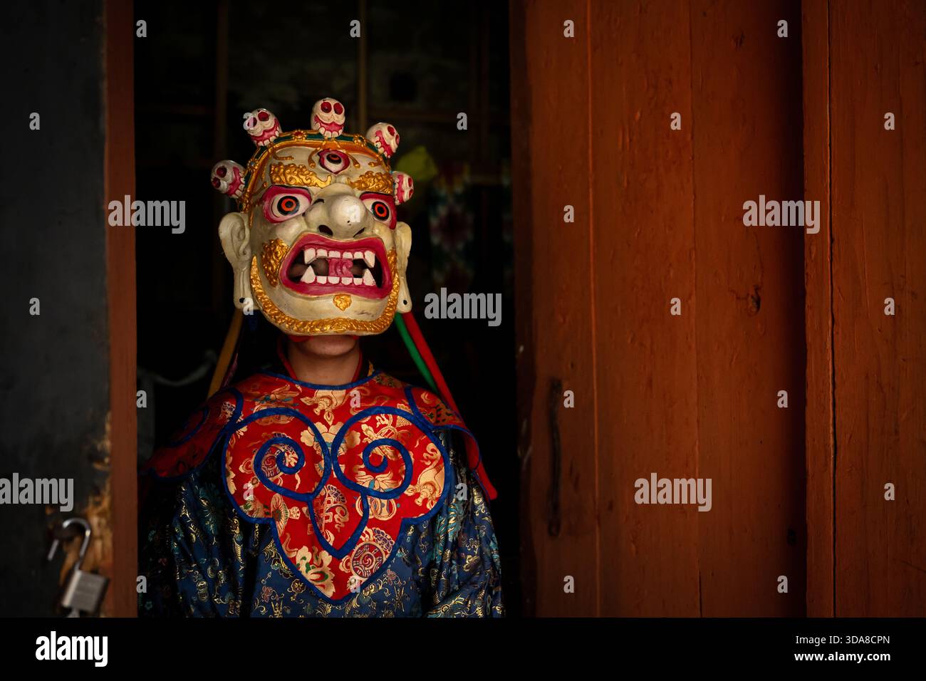 Jakar, Bhutan - 24. September 2025: Blick auf eine lebendige, aufwendig gestaltete Maske mit mehreren Augen und Schädeln, die sich im Kontrast zum dunklen Eingang und befindet Stockfoto