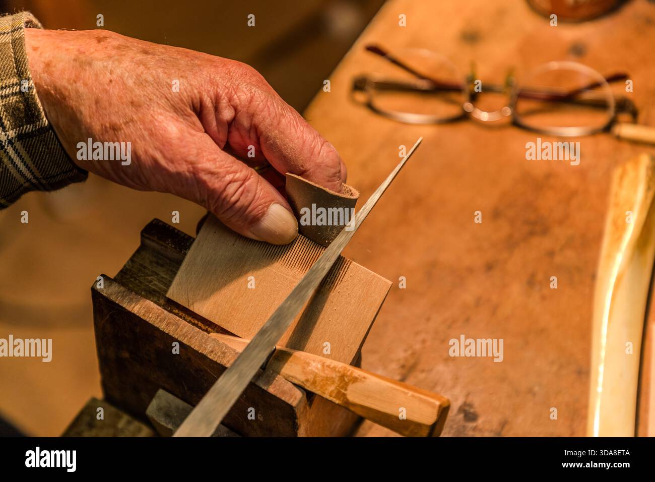 Ein Handwerker feilt in einer Werkstatt in Kiso, Präfektur Nagano, Japan, die Zähne eines geklemmten Holzkamms mit einer Nadelfeile. Im Hintergrund liegen eine Brille und ein halbfertiger Kamm Stockfoto