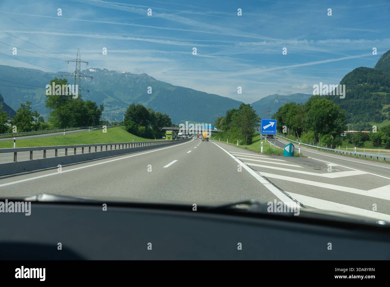 Eine saubere mehrspurige Autobahn, umgeben von Grün und Bergen unter einem hellblauen Himmel. Glatter Asphalt, klare Markierungen und malerische Natur machen das aus Stockfoto