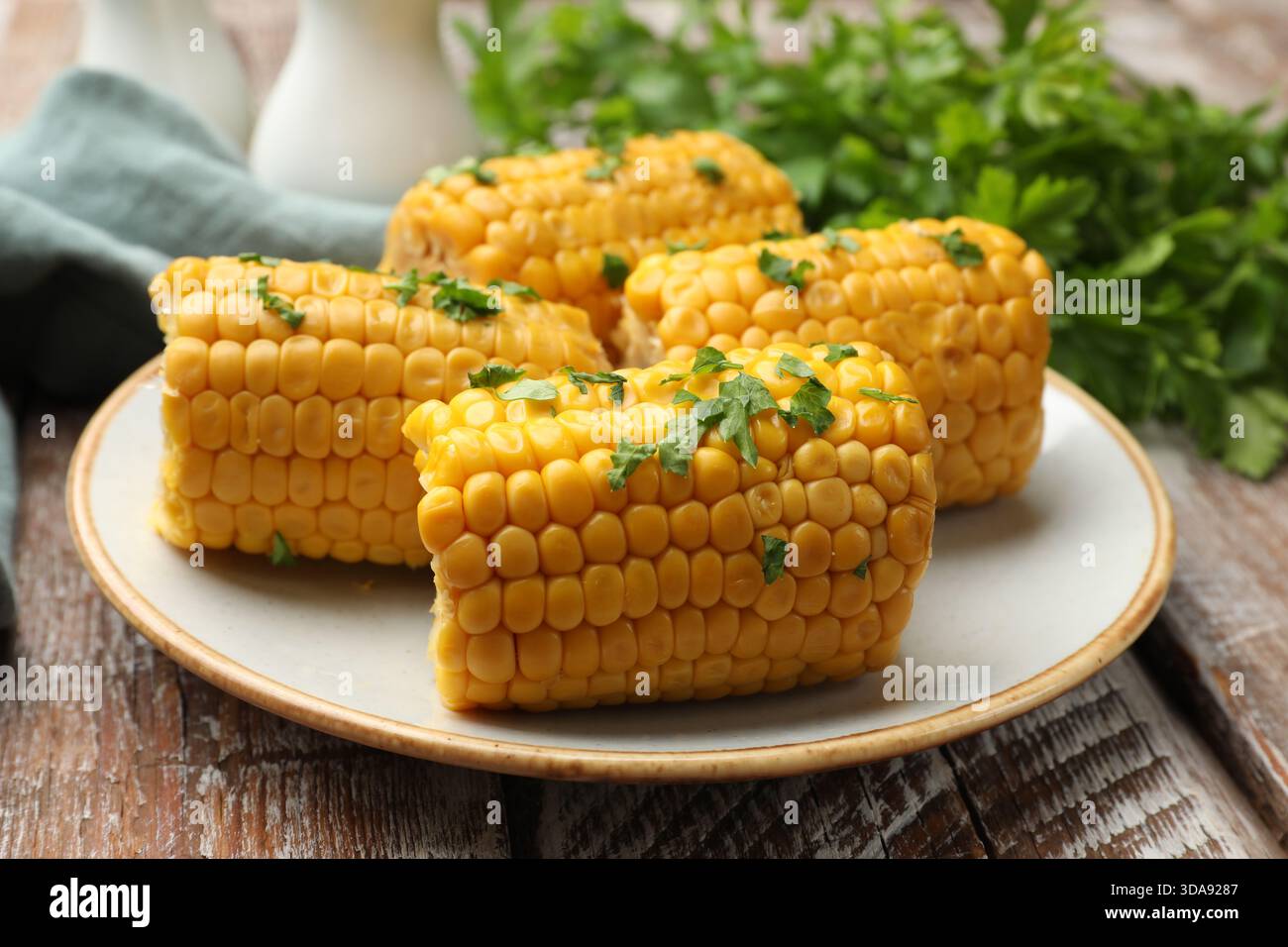 Stücke gekochter Maiskolben mit Petersilie auf Holztisch, Großaufnahme Stockfoto