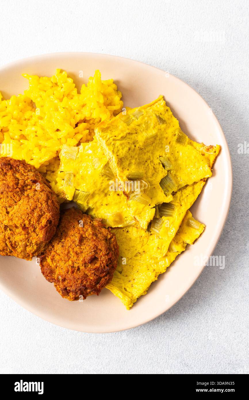 Ein lebhafter Teller mit flauschigem gelbem Reis, cremigen Rhabarber-Spiegeleiern und knusprigen Fleischgerichten bietet eine herzhafte und geschmackvolle Mahlzeit, die perfekt für einen ist Stockfoto