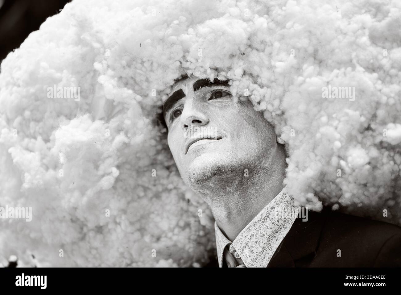 Schwarz-weiße Nahaufnahme eines männlichen Erwachsenen mit voluminöser Wolke - wie Kopfschmuck. Ausdruck wirkt kontemplativ und betont theatralisches A Stockfoto