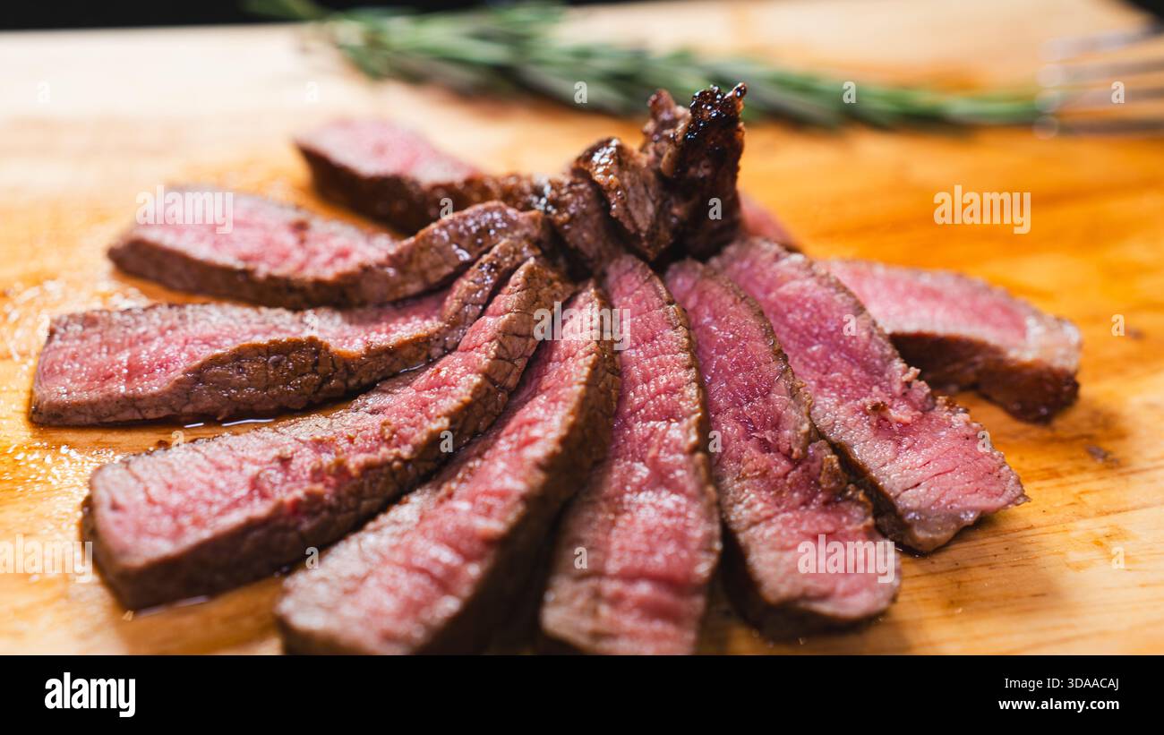 In Scheiben geschnittene, seltene Steaks auf einem Holzbrett mit Rosmarinzweigen. Rosafarbene Innenausstattung, goldene Kruste, saftig und perfekt gekocht. Elegante Fleischpräsentation Stockfoto