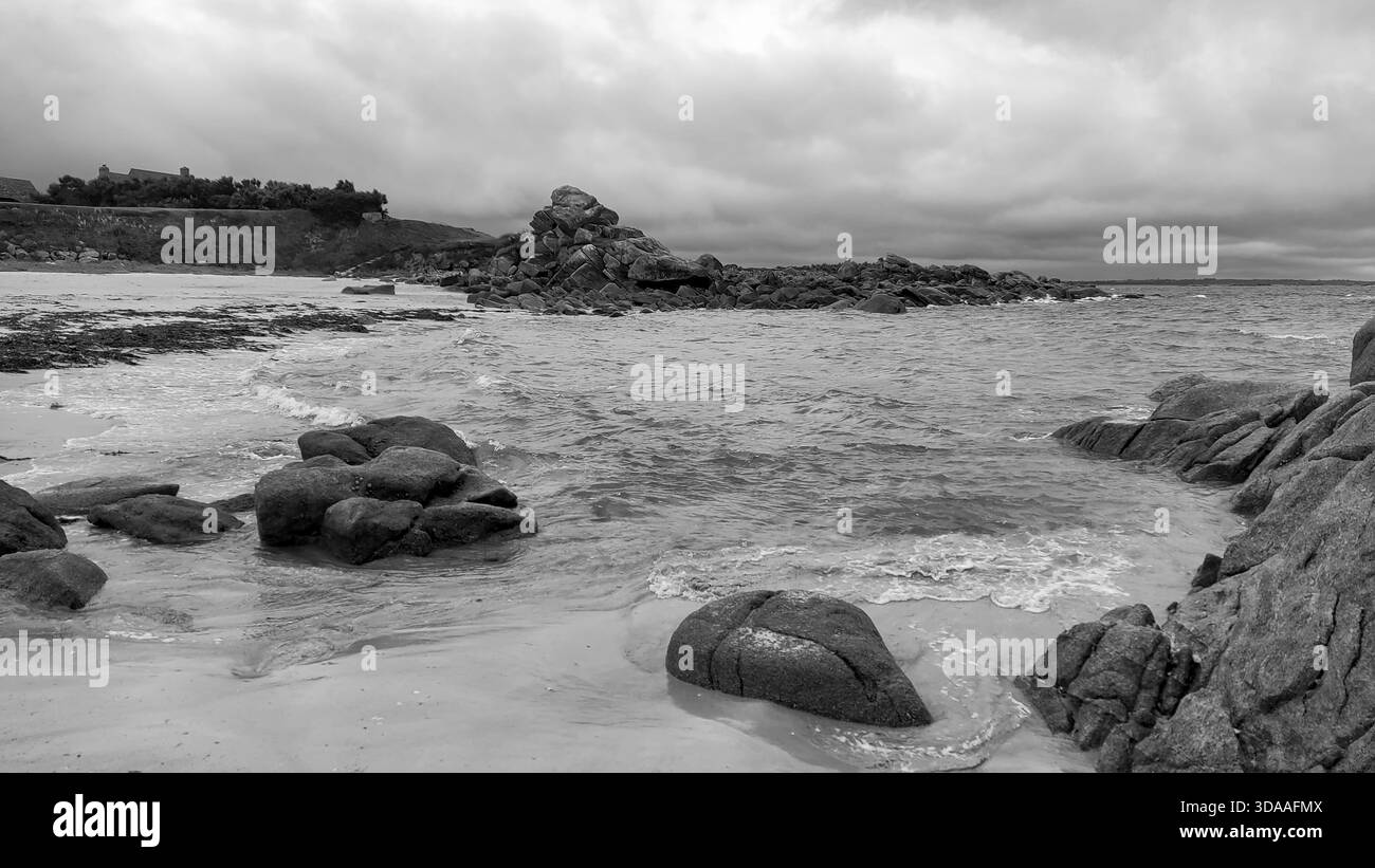 Schwarz-weiße zerklüftete Küstenlandschaft mit moosbedeckten Felsen unter bewölktem Himmel, die eine dramatische und natürliche Atmosphäre schaffen Stockfoto