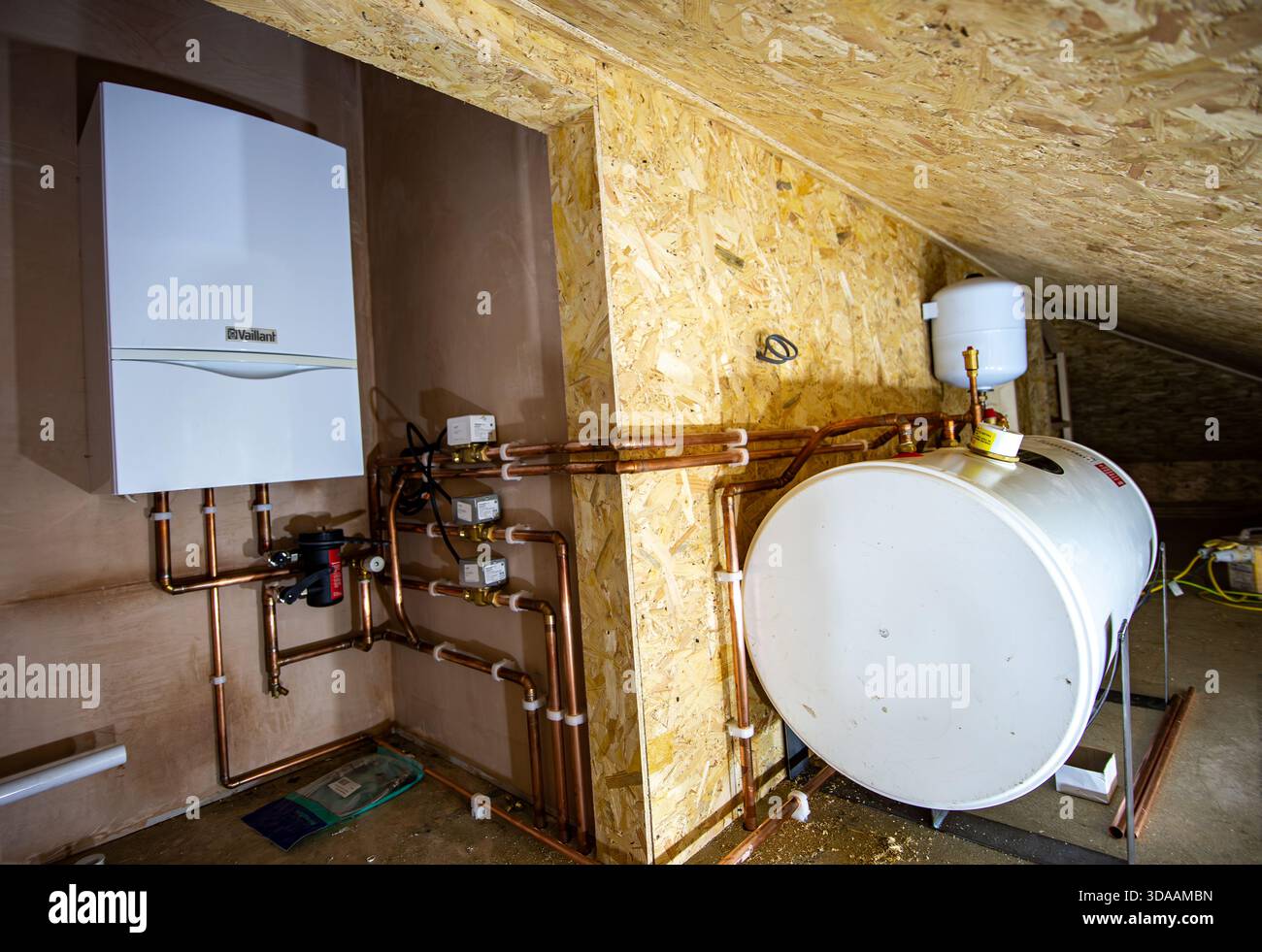 Modernes Kessel- und Warmwasserzylindersystem in einem Loft mit sichtbaren Kupferrohren und Dämmplatten Stockfoto