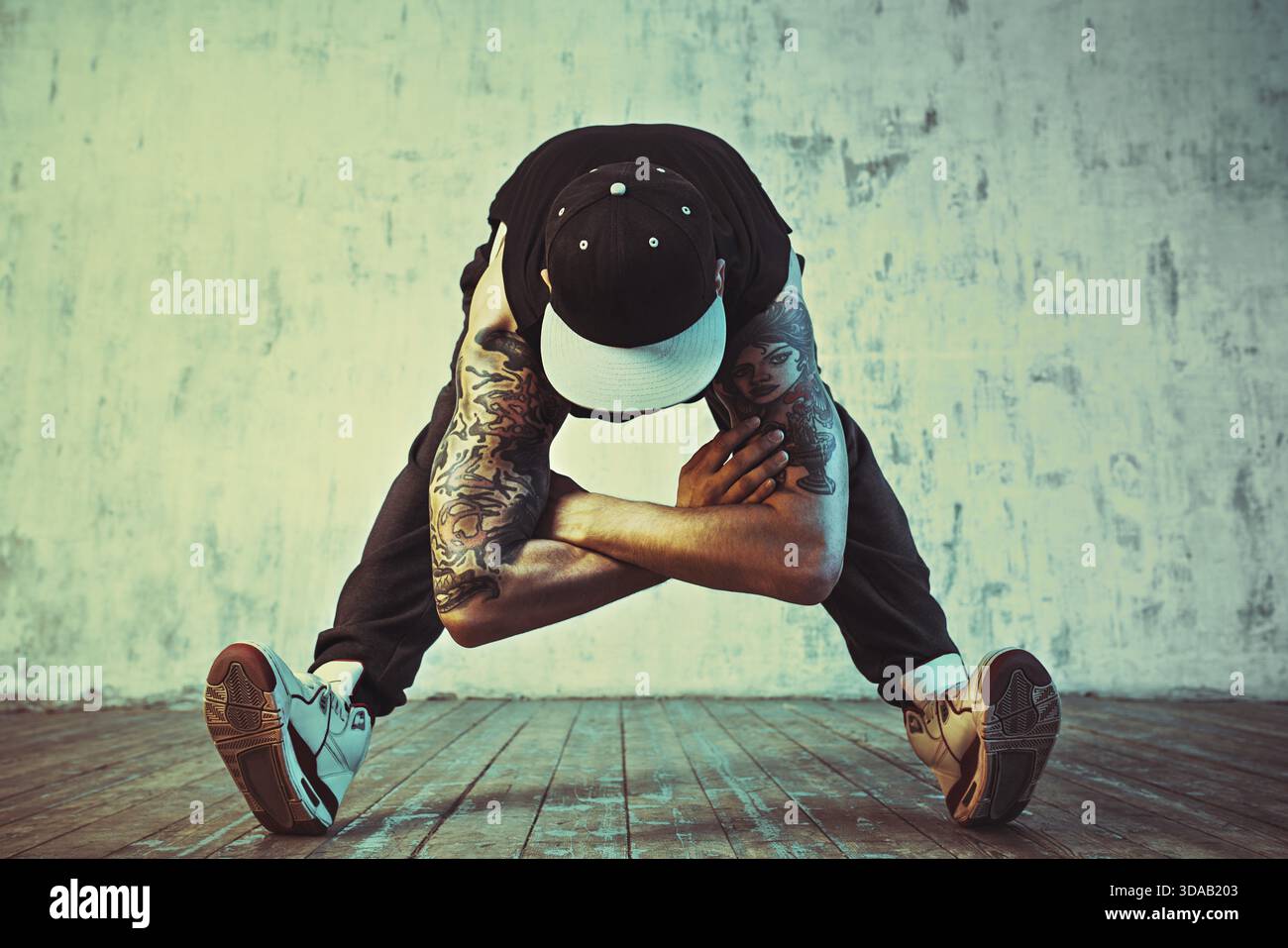 Junger Mann, der auf Wandhintergrund tanzt. Blaue und gelbe Farbtöne. Tätowierung am Körper Stockfoto