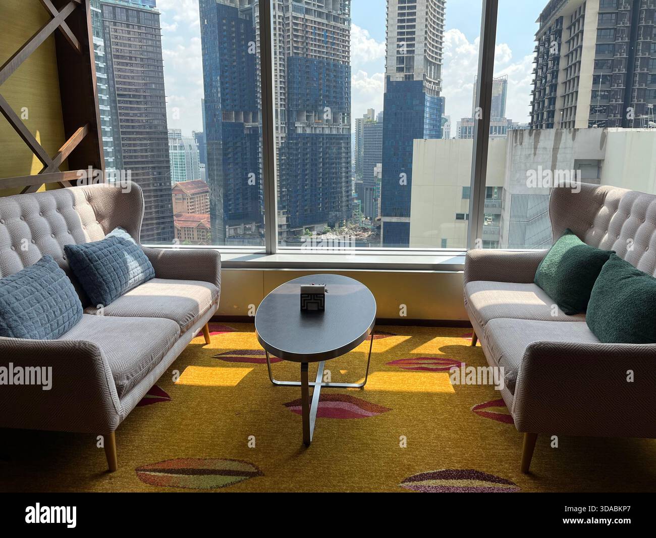 Moderne Lounge mit gemütlichen Sofas, lebhaftem Teppich und Panoramablick auf die Stadt, perfekt für Komfort und urbane Eleganz. Stockfoto