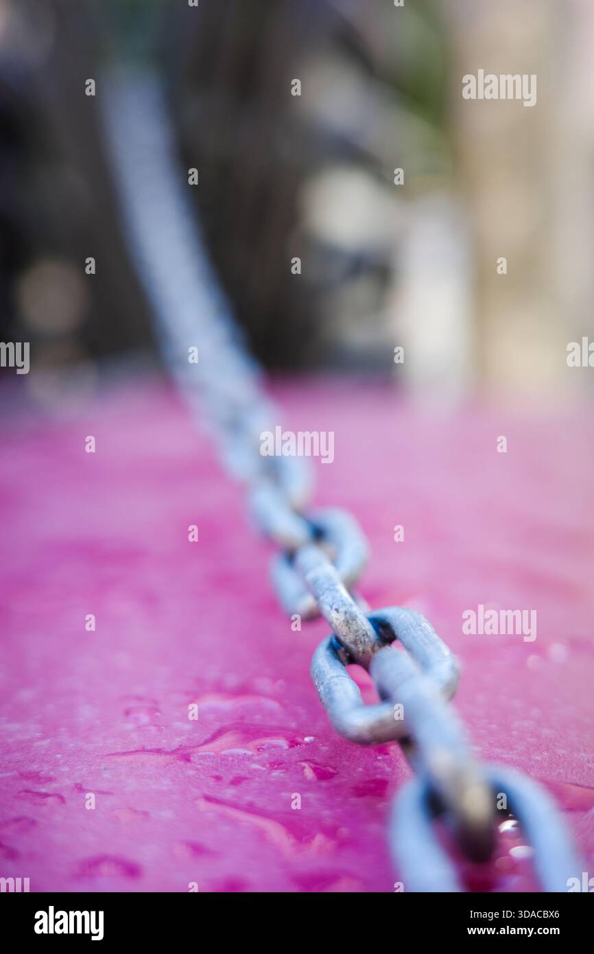 Metallkette auf nassrosa Oberfläche mit geringer Schärfentiefe Stockfoto