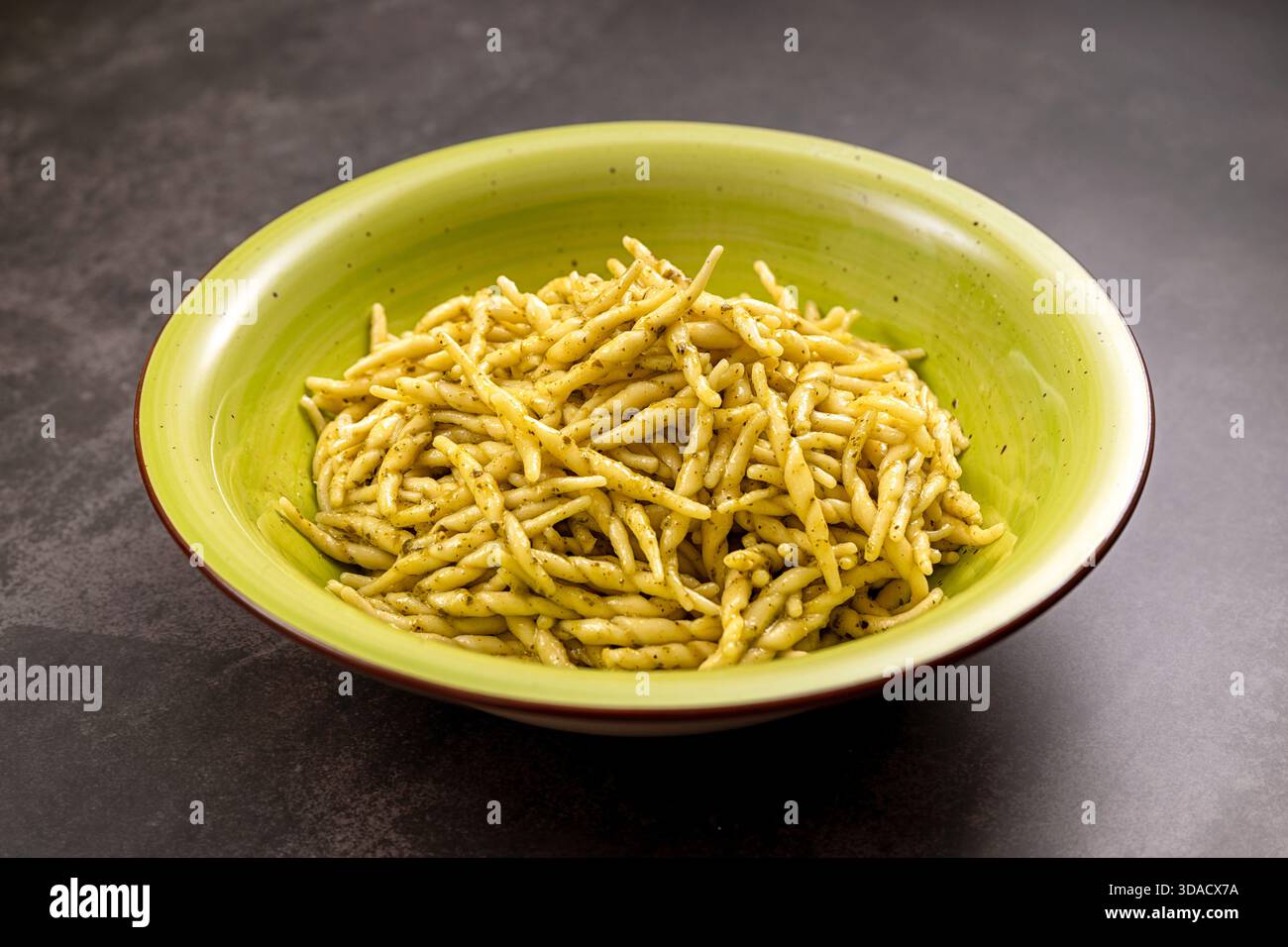 Trofie-Pasta mit grüner Pesto-Sauce in einer hellgrünen Schüssel, die italienische kulinarische Tradition repräsentiert Stockfoto