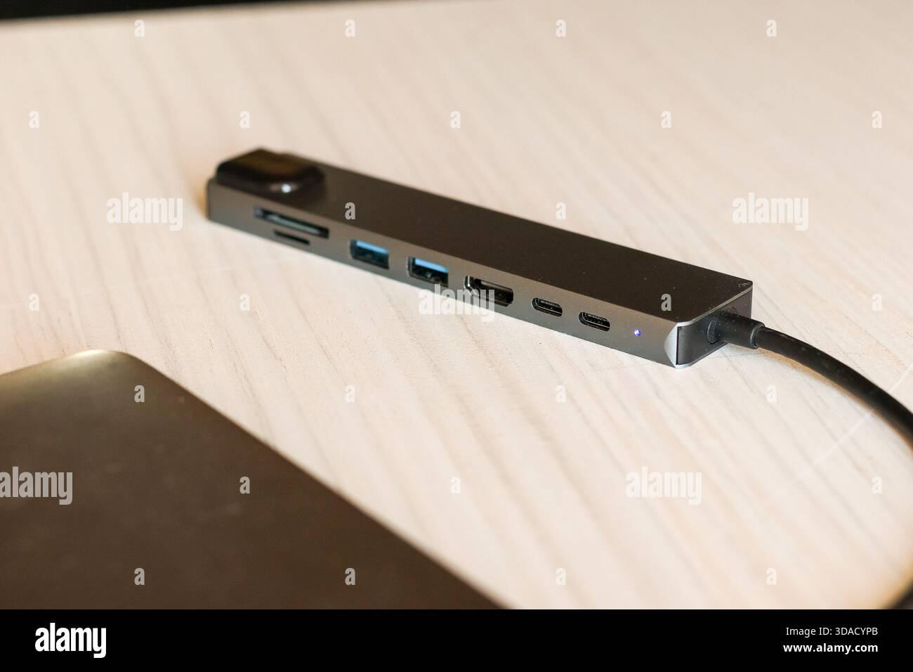 Vielseitiger grauer USB-C-Hub mit HDMI, USB-Anschlüssen und SD-Kartenleser, verbunden mit einem Laptop für erweiterte Konnektivität Stockfoto