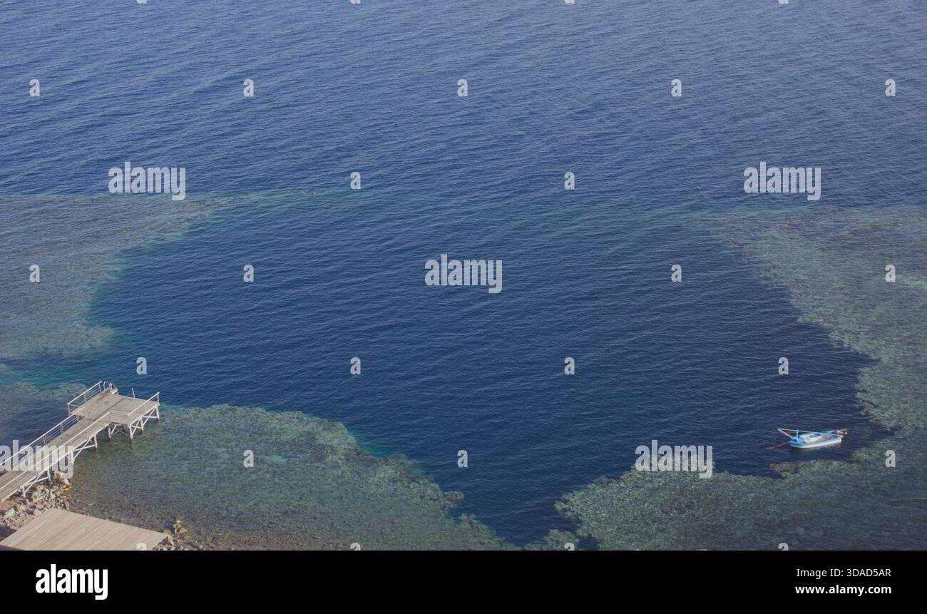 Blue Hole in Dahab, Ägypten, von oben gesehen mit Korallenriff und einem kleinen Boot auf klarem Wasser des Roten Meeres. Beliebter Ort zum Tauchen und Schnorcheln. Stockfoto