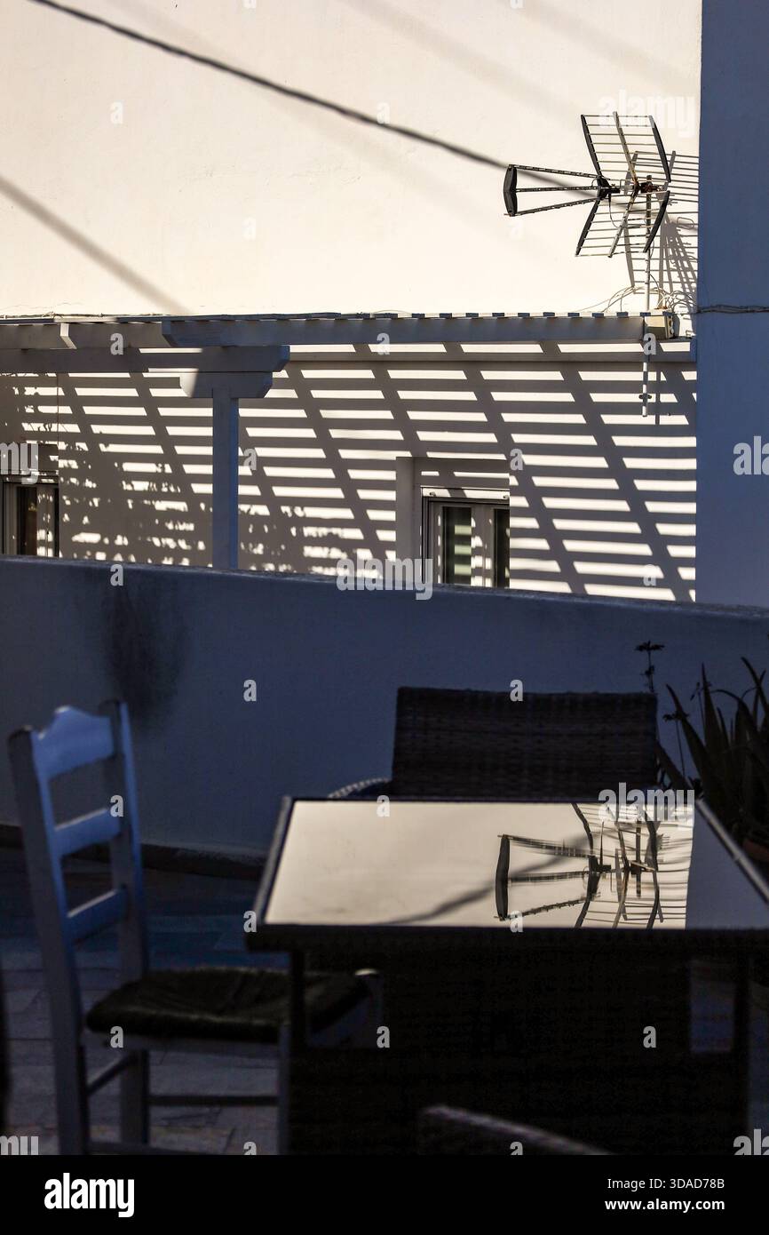 Eine minimalistische Outdoor-Szene mit einer weißen Wand mit starken linearen Schatten von einer Pergola und einer Antenne. Stockfoto