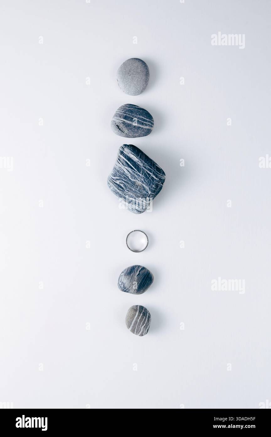 Blick von oben auf fünf verschiedene Steine und einen silbernen Ring, der in einer Reihe auf weißem Hintergrund angeordnet ist Stockfoto