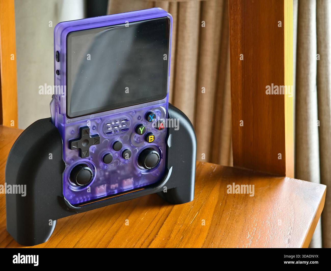 Badung, Bali, Indonesien - 29. November 2025 : R36S Handheld-Spielkonsole in transparenter violetter Farbe, in einem schwarzen Ständer oder Griffzubehör Stockfoto