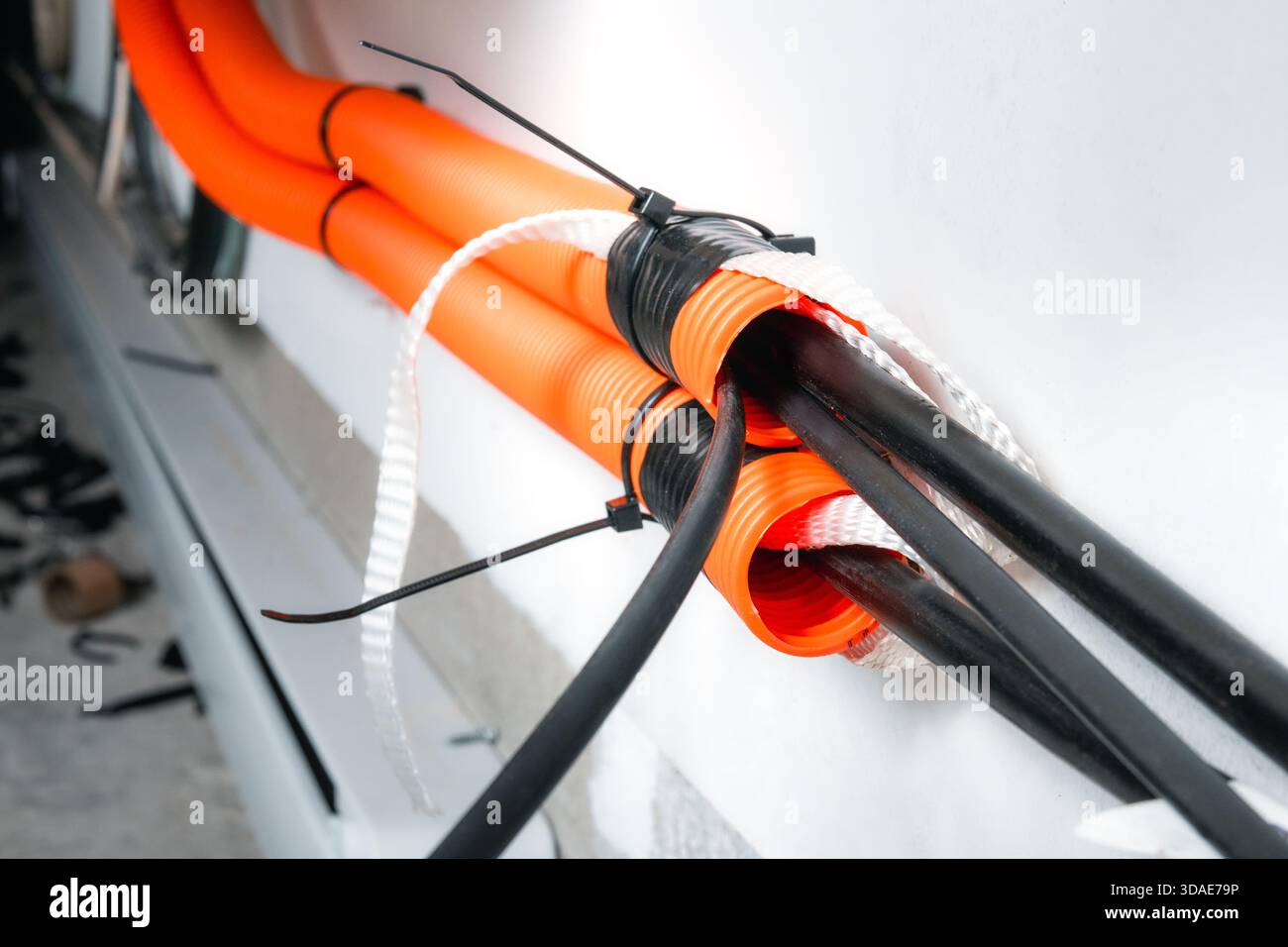 Innenkanal mit Glasfaserkabel. Oranges Rohr für Wandmontage mit Schnüren und losen Rohrkabeln. Kabelmanagement oder Kabelziehen in hoher Geschwindigkeit Stockfoto