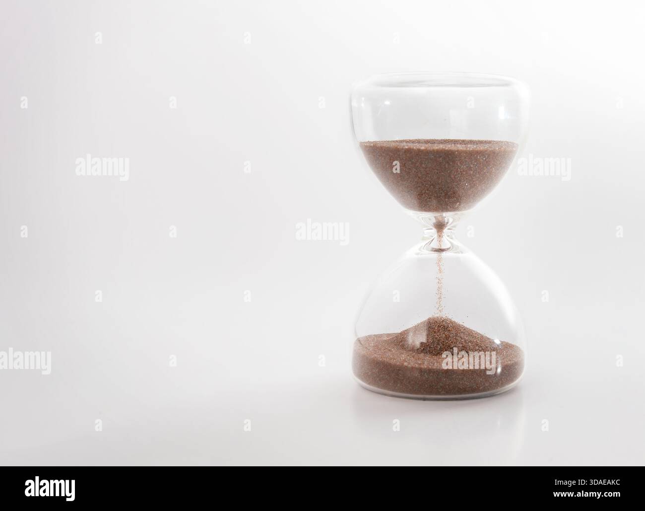 Sanduhr mit Sand auf grauem Hintergrund. Konzept für Zeitmanagement, Termin, Dringlichkeit oder Countdown. Sandglas halb leer mit fallendem Sand Stockfoto