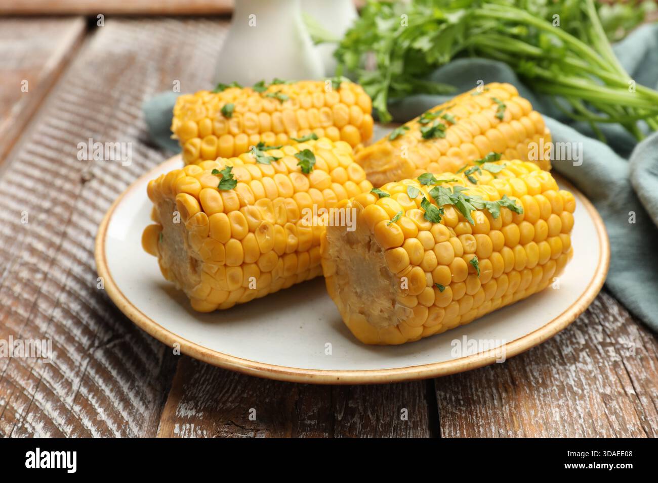 Stücke gekochter Maiskolben mit Petersilie auf Holztisch, Großaufnahme Stockfoto