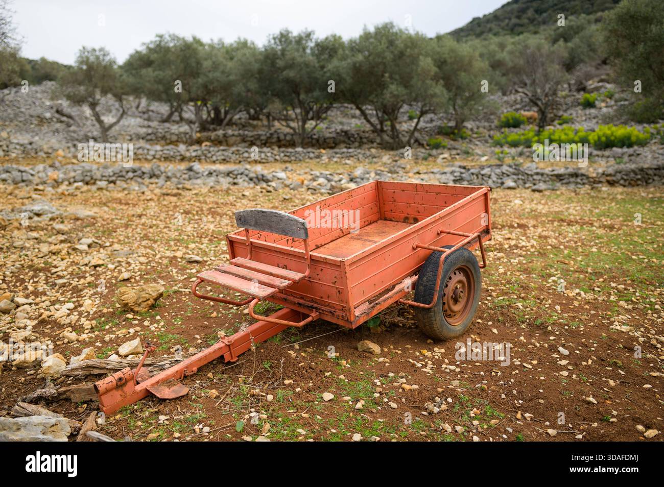 Ein orangener Anhänger steht auf einem kleinen Feld, umgeben von Steinmauern in Cres, Kroatien, der im Frühling in rustikaler Atmosphäre gefangen gehalten wird. Cres Kroatien Stockfoto