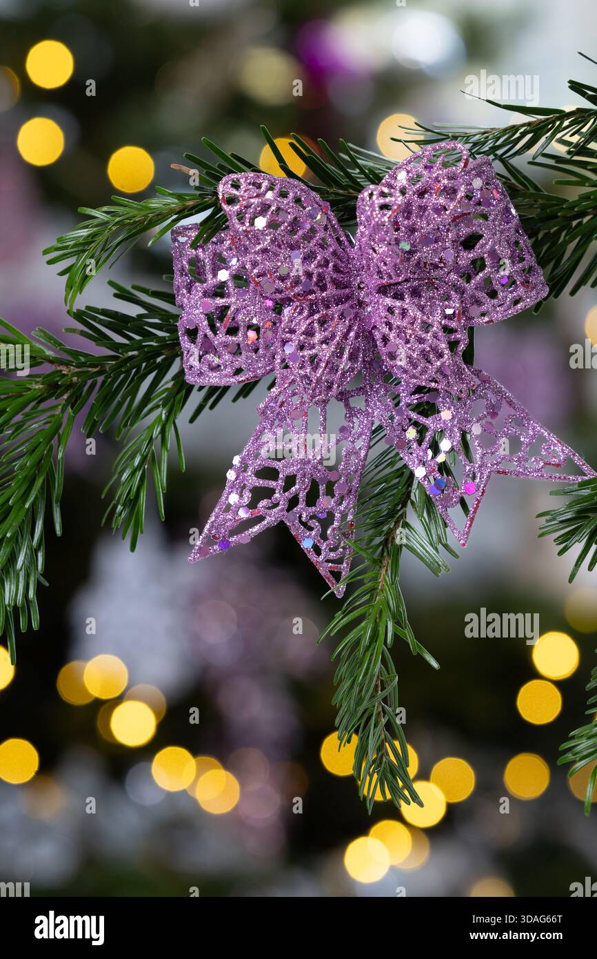 Lila Glitzer Schmetterlingsschmuck hängt an einem Tannenzweig mit warmen goldenen Bokeh-Lichtern im Hintergrund, elegante festliche Weihnachtsdekoration Stockfoto
