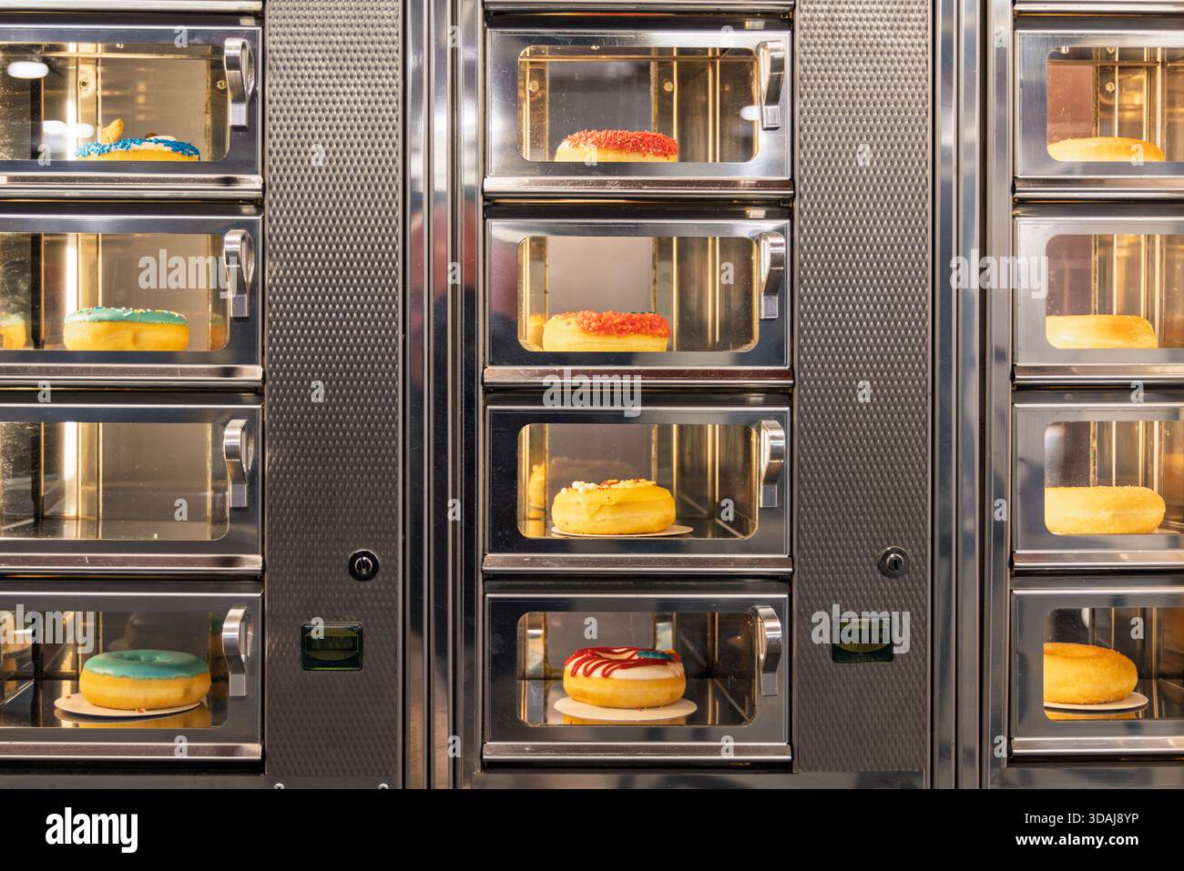 Automaten mit verschiedenen bunten glasierten Donuts hinter Glastüren, die süße Köstlichkeiten zum Verkauf in einem öffentlichen Einkaufsviertel anbieten. Stockfoto