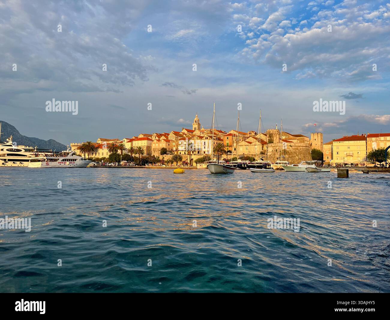 Goldenes Abendlicht über der Altstadt von Korčula, wo Steinmauern auf das ruhige Blau der Adria treffen. - Smartphone-aufgenommenes Stockfoto