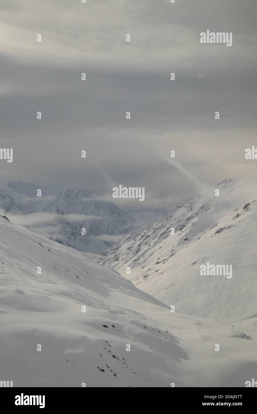 Sanftes Licht über einem schneebedeckten Bergtal mit niedrigen hängenden Wolken und Nebel Stockfoto