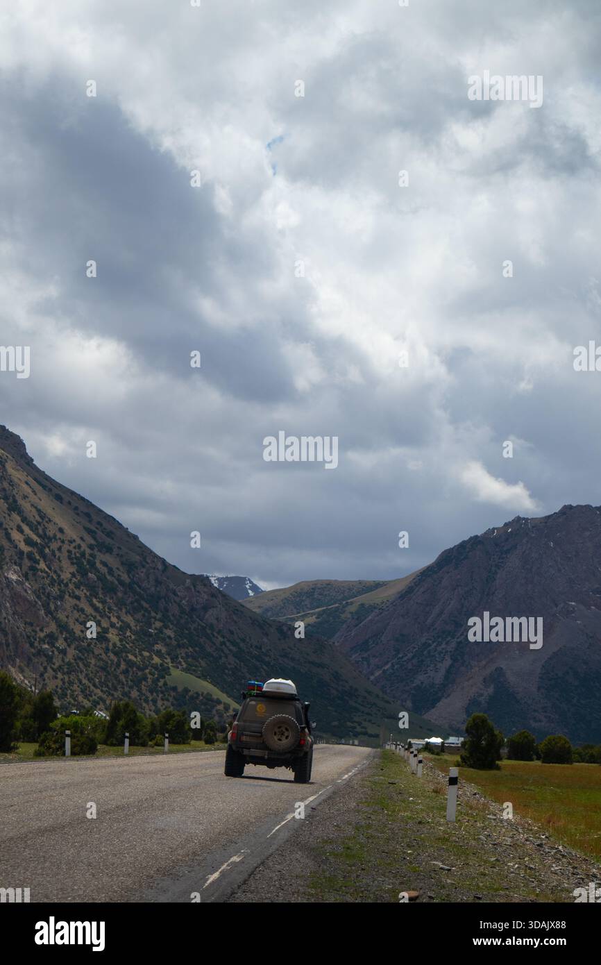 Rückansicht eines Geländewagens mit Dachträger, der auf der Bergstraße unter stimmungsvollem Himmel fährt Stockfoto