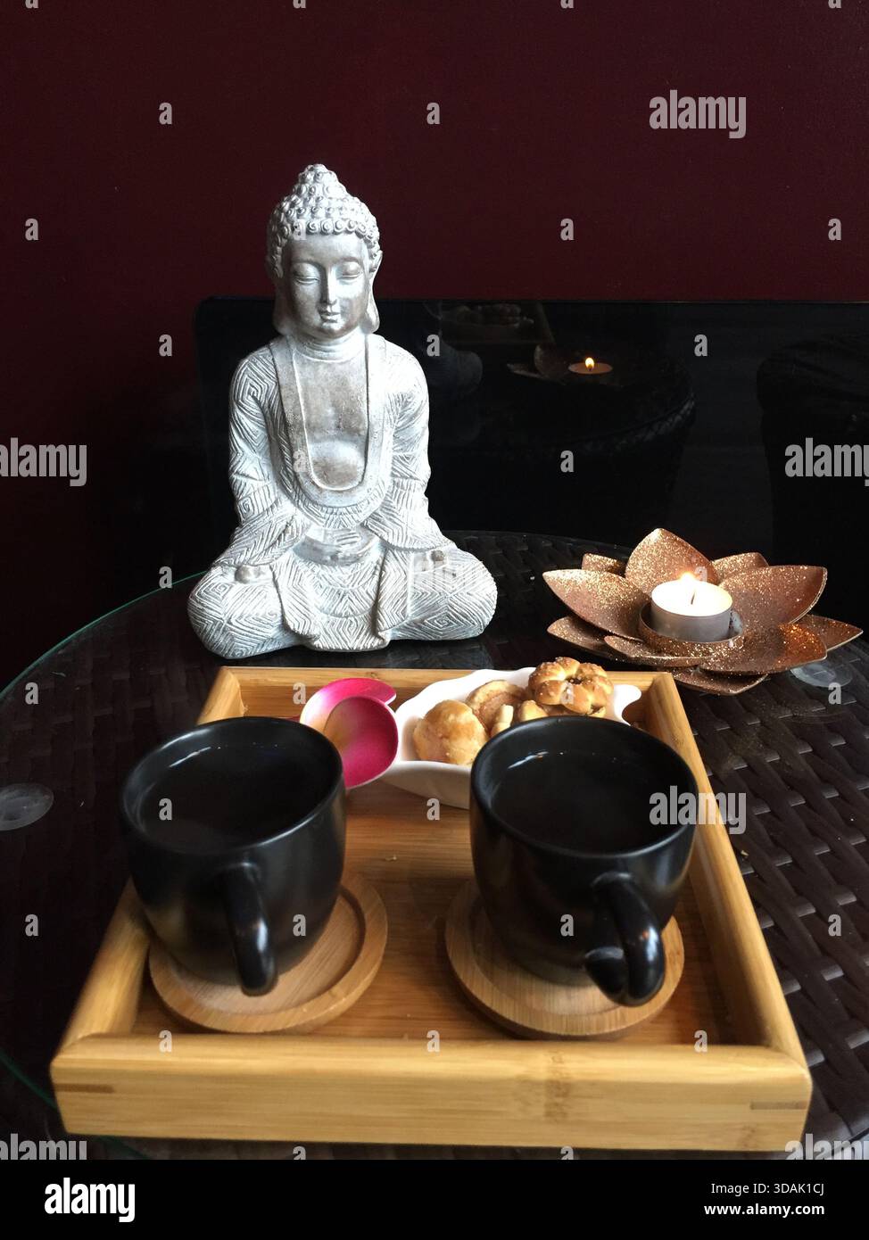 Teetassen und Kekse, Buddha-Statue und Kerze auf künstlicher Lotusblume Stockfoto