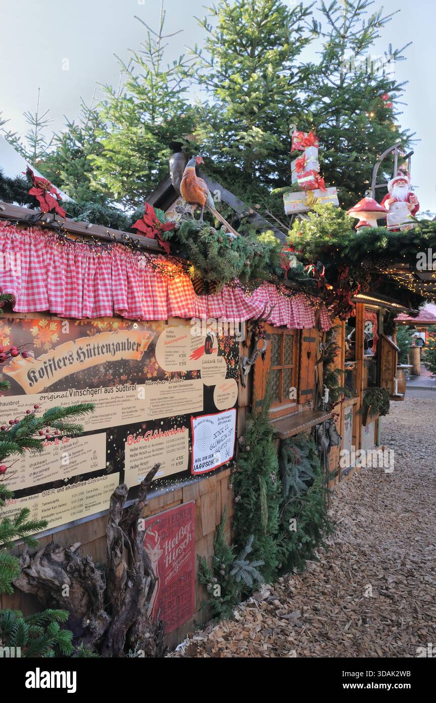 Weihnachtsmarkt-Hütte mit immergrünen Zweigen, Lichterketten und rot-weiß karierten Stoffen. Auf dem Dach befinden sich festliche dekorative Figuren, Stockfoto