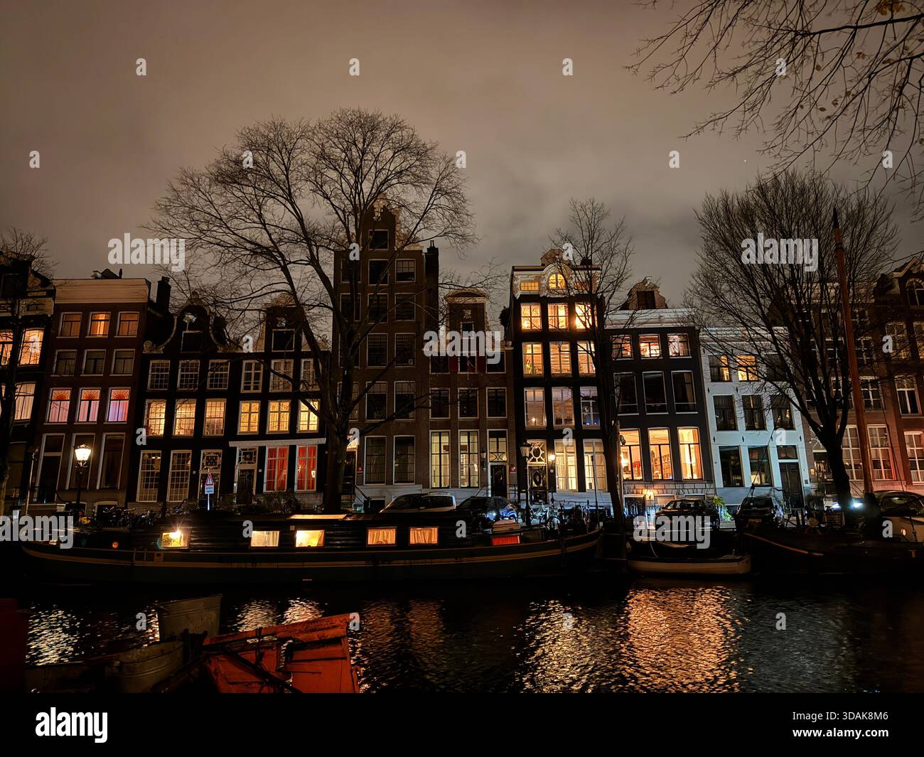 Beleuchtete Kanalhäuser entlang eines Amsterdamer Kanals bei Nacht - Smartphone-aufgenommenes Stockfoto