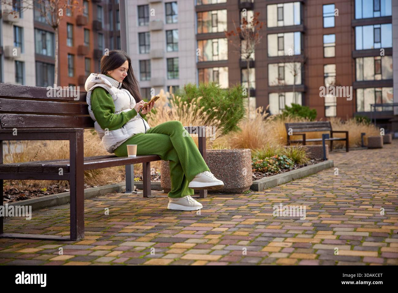 Frau, die auf einer Parkbank sitzt und auf ihrem Handy SMS schreibt Stockfoto