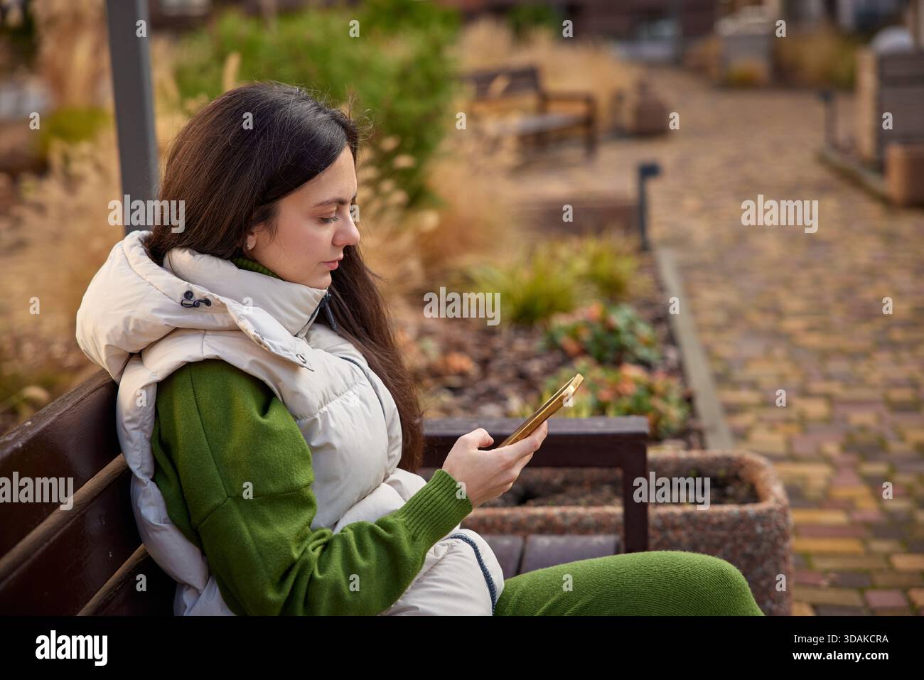 Frau, die auf einer Parkbank sitzt und auf ihrem Handy SMS schreibt Stockfoto