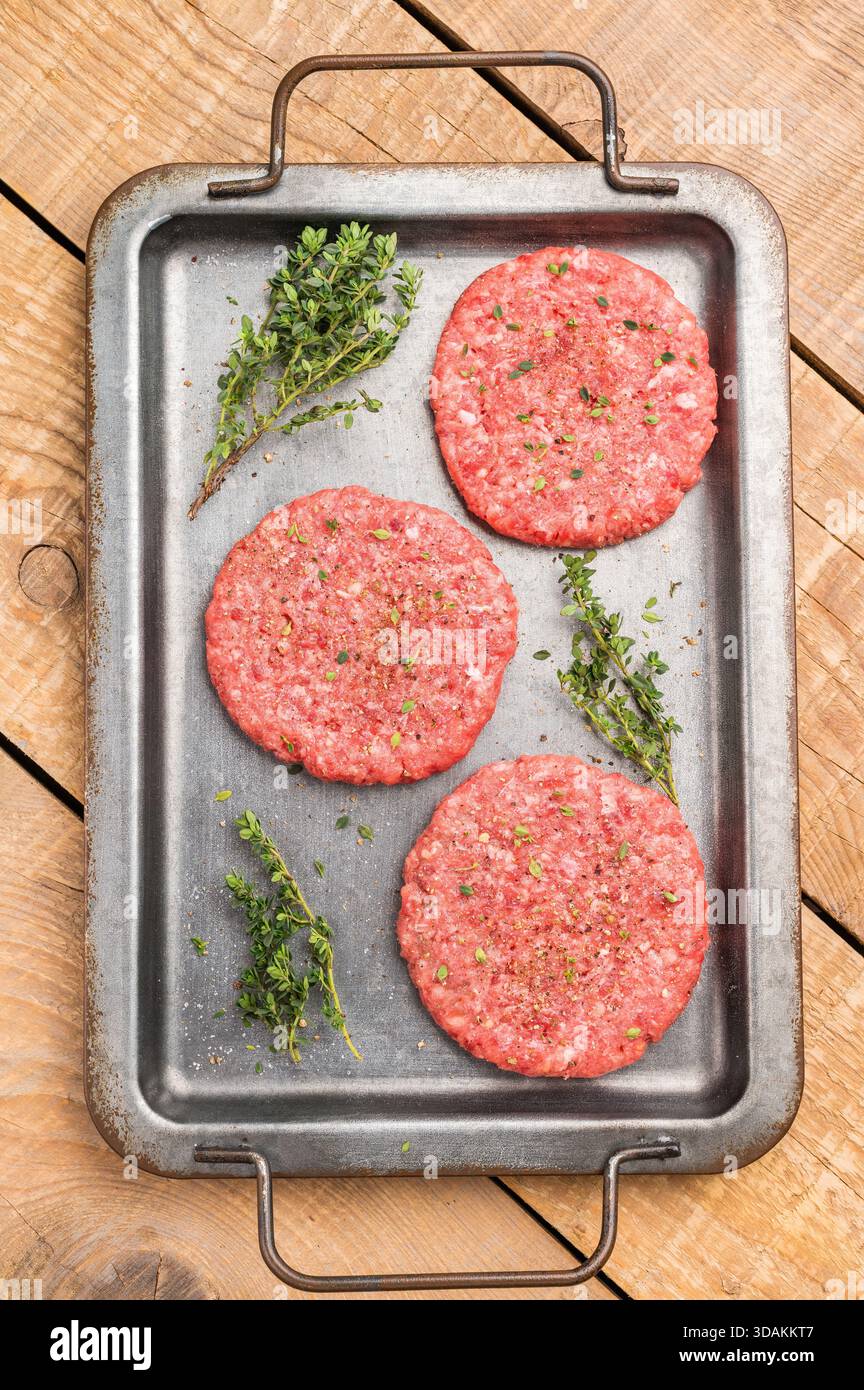 Rohe Hamburger Hackfleischpasteten für Burger mit Kräutern auf Tablett. Hölzerner Hintergrund. Draufsicht Stockfoto