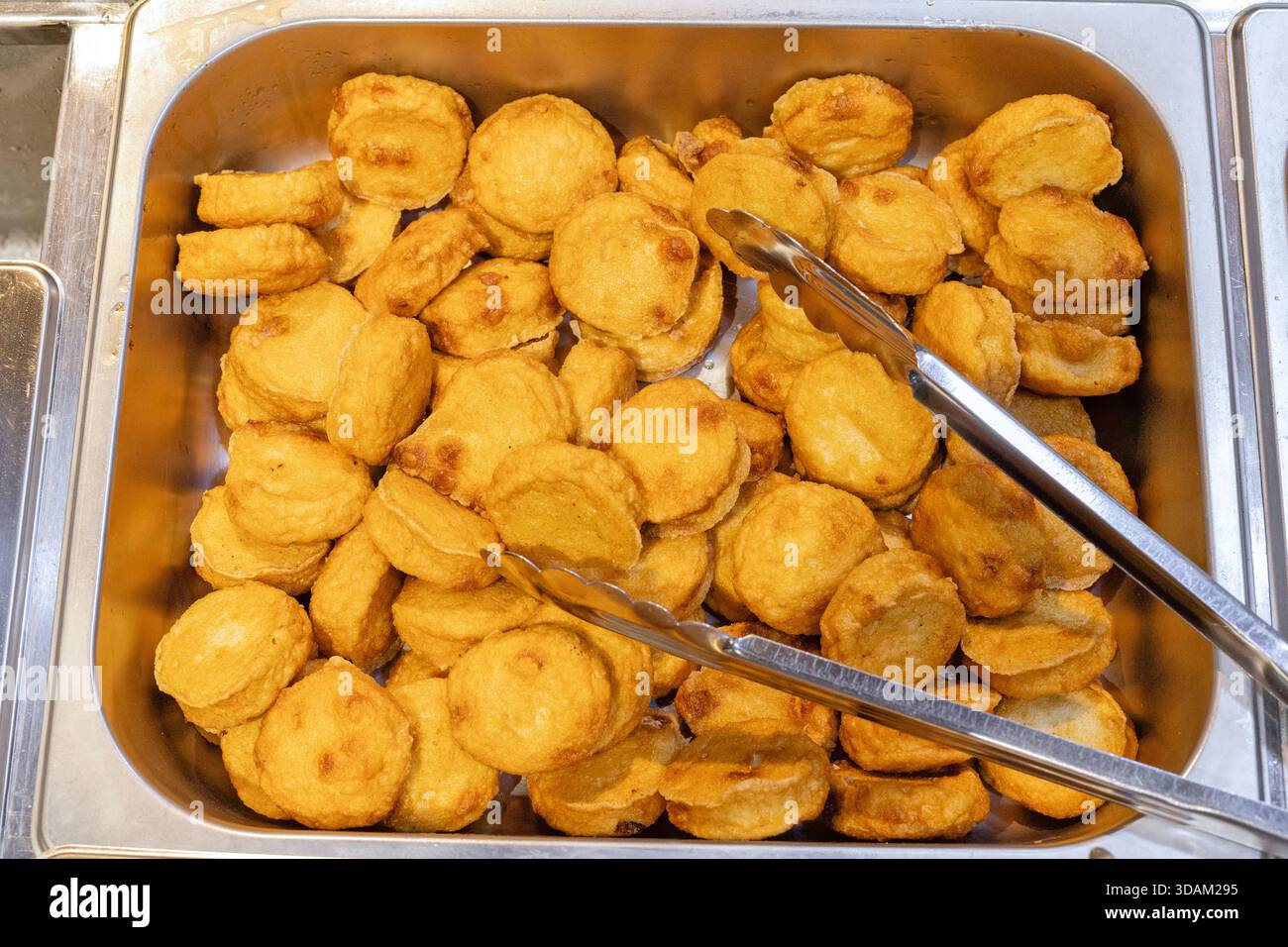 Aus nächster Nähe sehen Sie ein großes Metalltablett, das mit zahlreichen goldbraunen, runden, frittierten Fischkuchen gefüllt ist und servierfertig ist Stockfoto