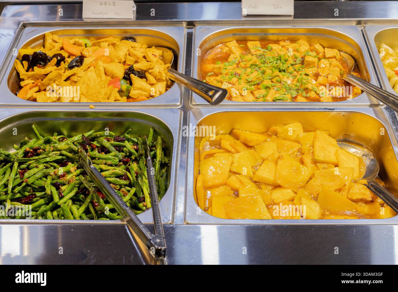 Aus nächster Nähe sehen Sie ein Buffet mit mehreren Edelstahltabletts, gefüllt mit verschiedenen asiatischen Gerichten, servierfertig Stockfoto