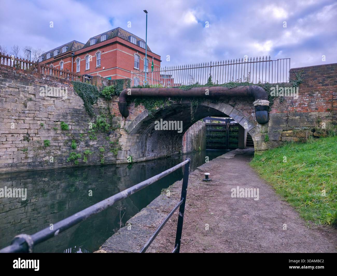 Historische Steinkanalbrücke mit großem Überlaufrohr und Schleusentoren auf dem Stroudwater Canal, Blick vom Schleppweg an einem bewölkten Wintertag, Stroud, Stockfoto