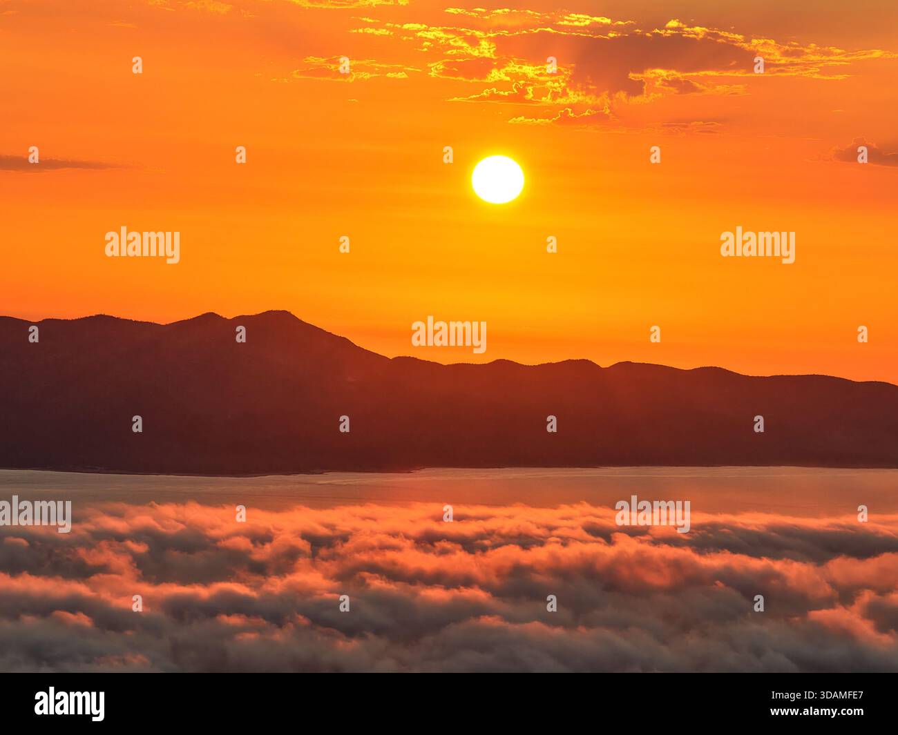 Aus der Vogelperspektive auf die Sonne über den Bergen am Horizont mit den Wolken darunter, La Paz, Baja California Sur, Mexiko. Stockfoto