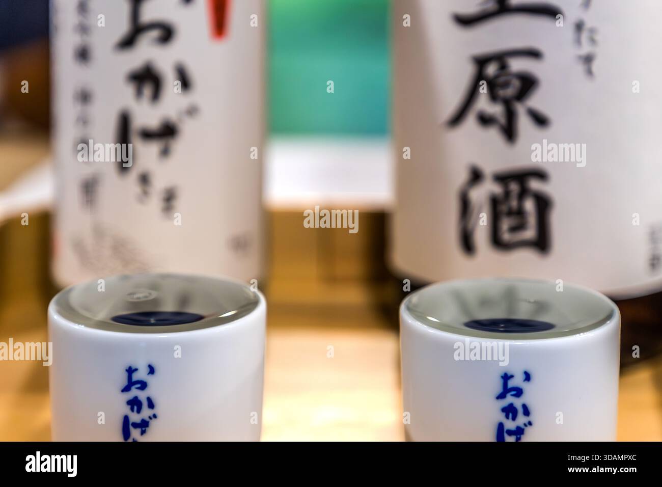 Eine Keramik Tasse, ein Ochoko und eine Flasche Namazake von der Okage Brauerei stehen in Oharai-machi, Ise, Präfektur Mie, Japan. Der Markenname Okage bezieht sich auf die Okagemairi-Massenpilgerreisen zum Ise-jingū während der Edo-Zeit sowie auf den Ausdruck Okage-sama de, „dank der Gnade der Götter“. Die Brauerei befindet sich direkt vor dem Eingang zum Naikū. Stockfoto