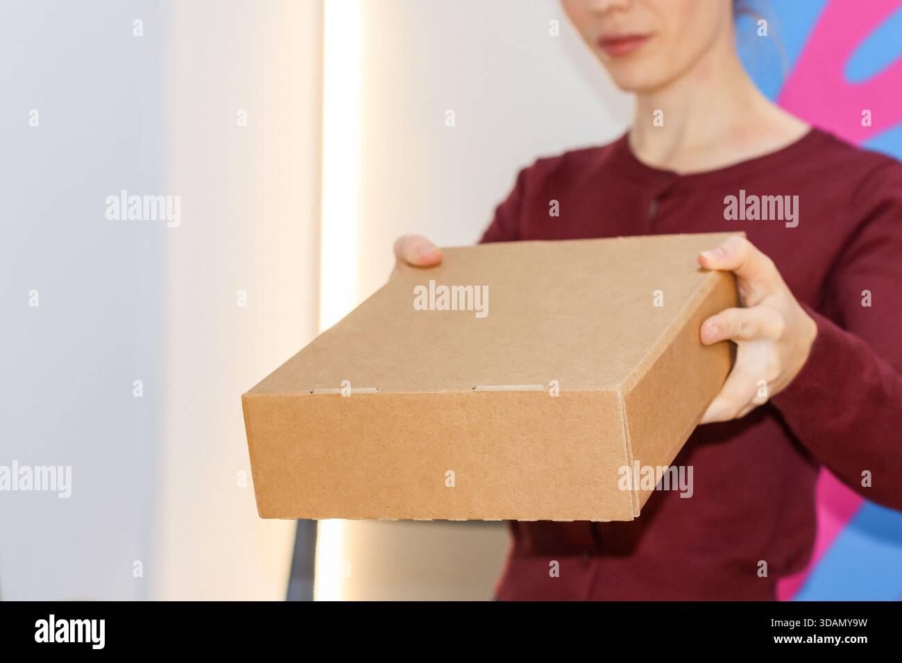 Der Abholmitarbeiter hält braune Pakete vor einer lebendigen Kulisse an der Abholstelle Stockfoto