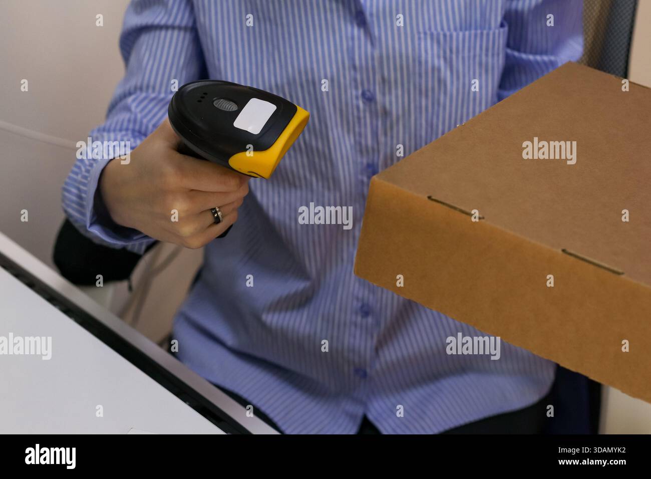Person in blau gestreiftem Hemd mit gelbem Scanner auf brauner Verpackung auf weißer Oberfläche Stockfoto