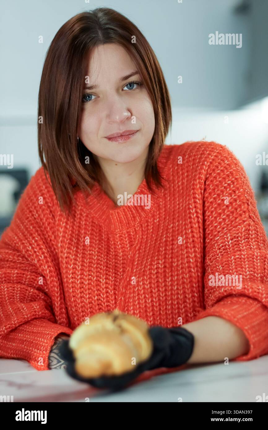 Neutraler Ausdruck im weiblichen Gesicht, da sie gebackenes Croissant mit Belag im Café-Arbeitsbereich anbietet. Stockfoto