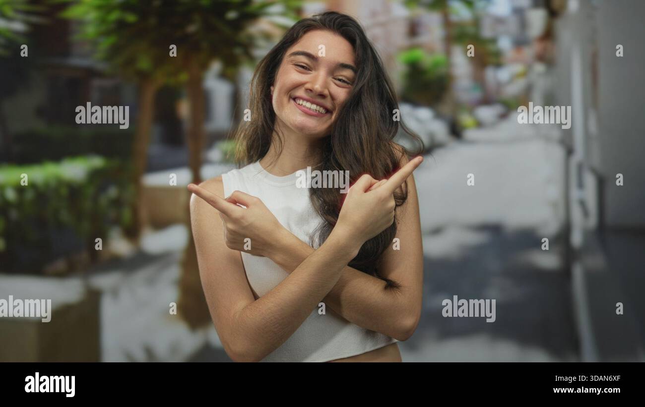 Junge Frau, die mit dem Finger in entgegengesetzte Richtungen an einer sonnendurchfluteten Straßenecke zeigt, die mit Topfpflanzen gesäumt ist; Orientierungsrichtung Klarheit Optimismus. Stockfoto