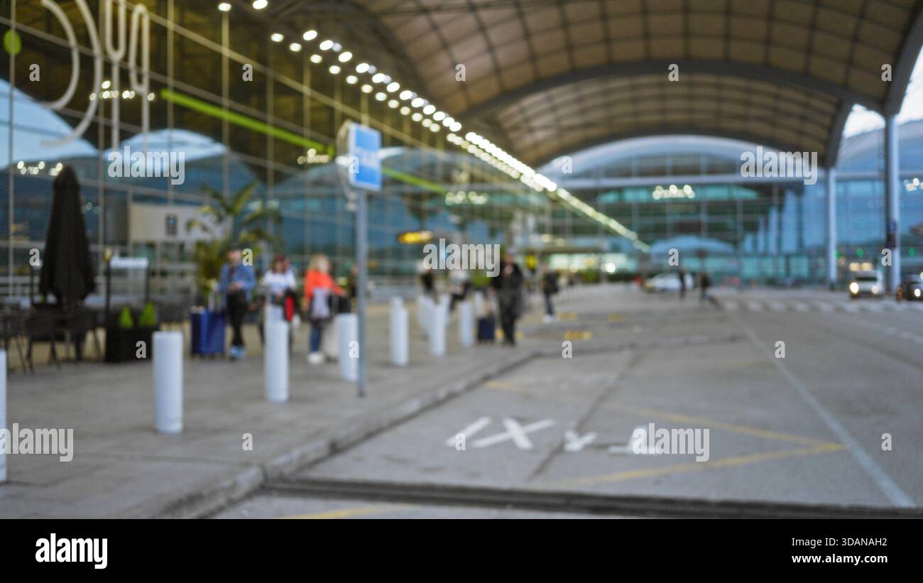 Flughafenterminal mit verschwommenen Reisenden im Freien in defokussiertem Hintergrund mit moderner Architektur und Bokeh-Beleuchtung in Terminal 1-Umgebung. Stockfoto