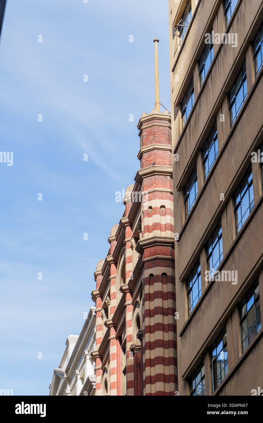 Ein flaches urbanes Bild, das die unterschiedlichen Stile eines historischen roten Backsteingebäudes und einer modernen braunen Fassade unter einem klaren blauen Himmel festlegt. Stockfoto