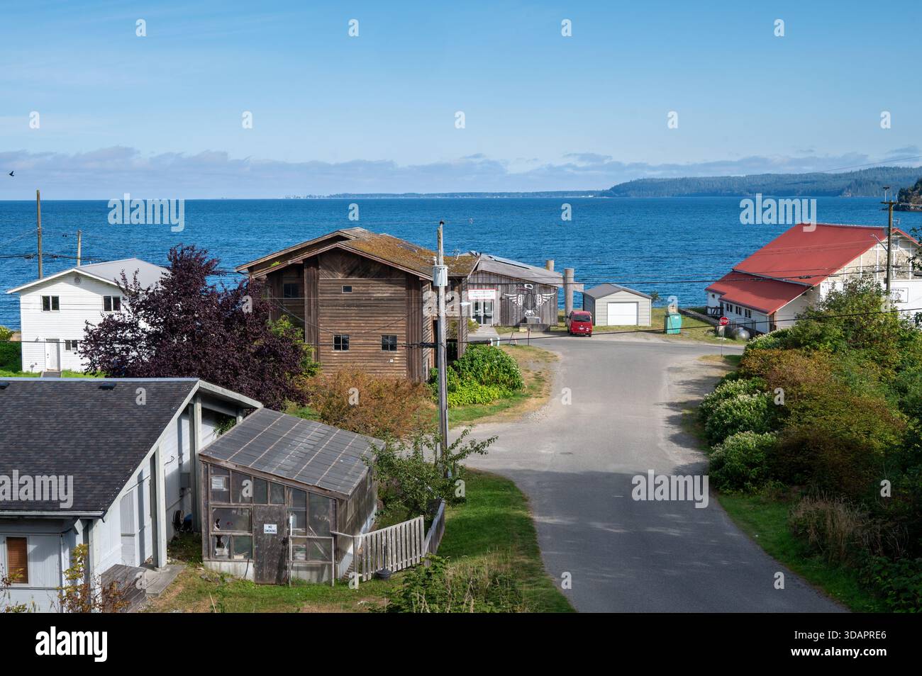 Straße, die durch ein Wohnviertel in Richtung Jugendzentrum und Meer in Skidegate, Haida Gwaii führt. Stockfoto