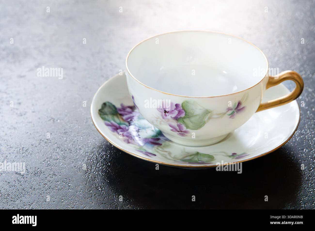 Leere Teetasse und Untertasse mit lilafarbenen Blüten bemalt, Kopierraum links Stockfoto