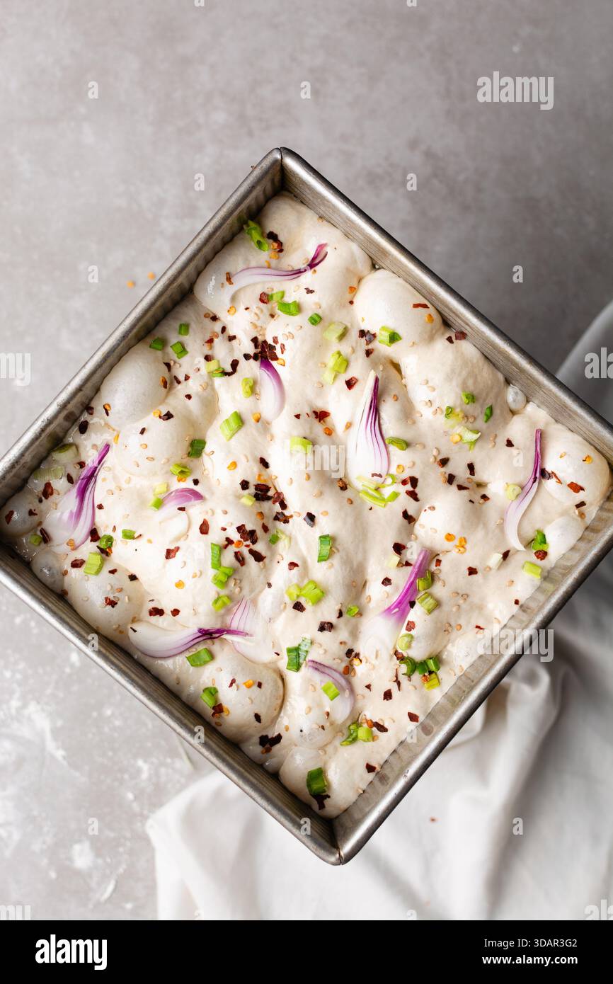 Draufsicht von Zwiebeln- und Schalottenfokaccia-Teigscheiben in einer quadratischen Backform, Draufsicht von luftiger, sprudelnder Zwiebelfokaccia-Teigprobung Stockfoto