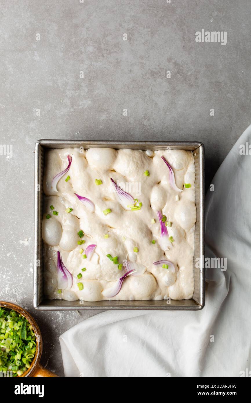 Draufsicht von Zwiebeln- und Schalottenfokaccia-Teigscheiben in einer quadratischen Backform, Draufsicht von luftiger, sprudelnder Zwiebelfokaccia-Teigprobung Stockfoto