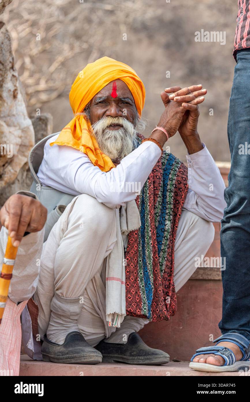 Älterer indischer Mann in Gelb Turban hockt draußen mit buntem gewebtem Tuch. Pushkar, Rajasthan, Indien, 28. Januar '24. Stockfoto