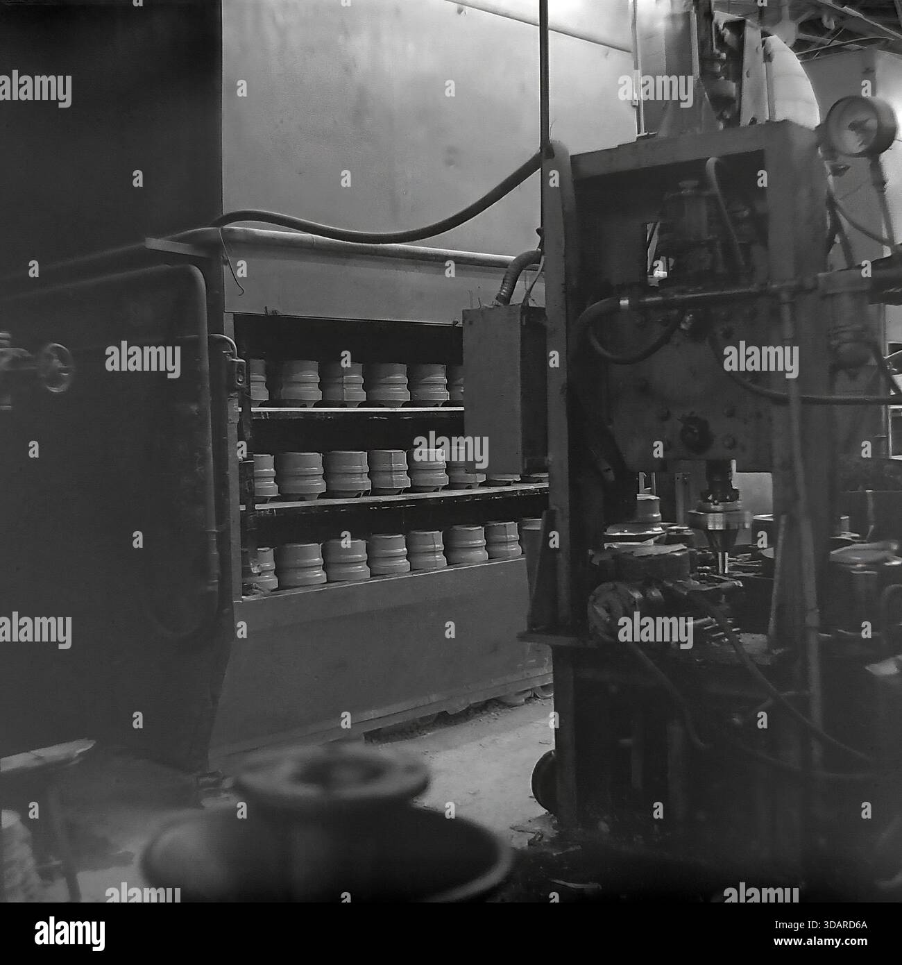 Slawjansk, Ukrainische SSR, 1980er Jahre Eine archivierte Innenansicht der Pressabteilung des Armature-Isolator Plant (AIZ). Rechts steht eine große vertikale Hydraulikpresse mit Manometern zur Formung von Hochspannungskomponenten. Auf der linken Seite ist eine Batch-Trockenkammer mit Einlegeböden aus rohen Keramikstiften (Modell Shy-20) gefüllt, die für die Wärmebehandlung vorbereitet werden. Dieses Bild zeigt die schweren Maschinen und technologischen Schritte in der friedlichen Donbass-Region. Stockfoto